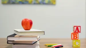Czerwone jabłko na stosie książek obok kolorowych klocków z literami alfabetu.