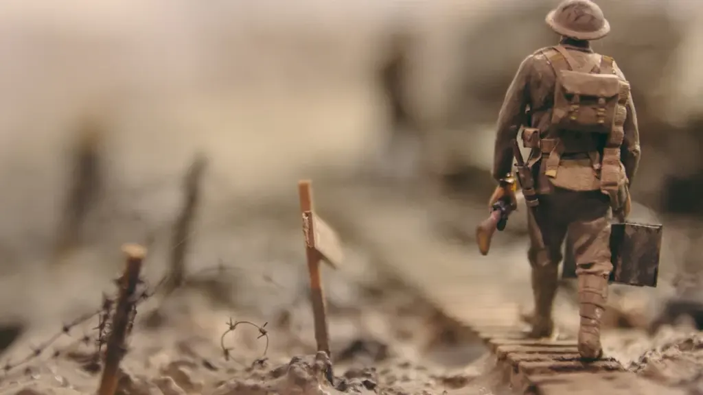 Figurka żołnierza krocząca wzdłuż zasieków w symbolicznej scenerii historycznej bitwy wojskowej.