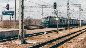 Pociąg pasażerski przejeżdżający przez stację kolejową w Trzebini w słoneczny dzień.