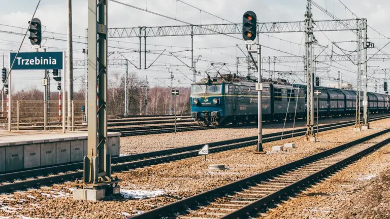 Pociąg pasażerski przejeżdżający przez stację kolejową w Trzebini w słoneczny dzień.