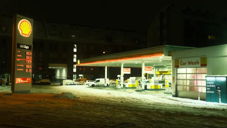 Oświetlona stacja paliw w nocy podczas zimy, zachęcająca do tankowania poza główną trasą.